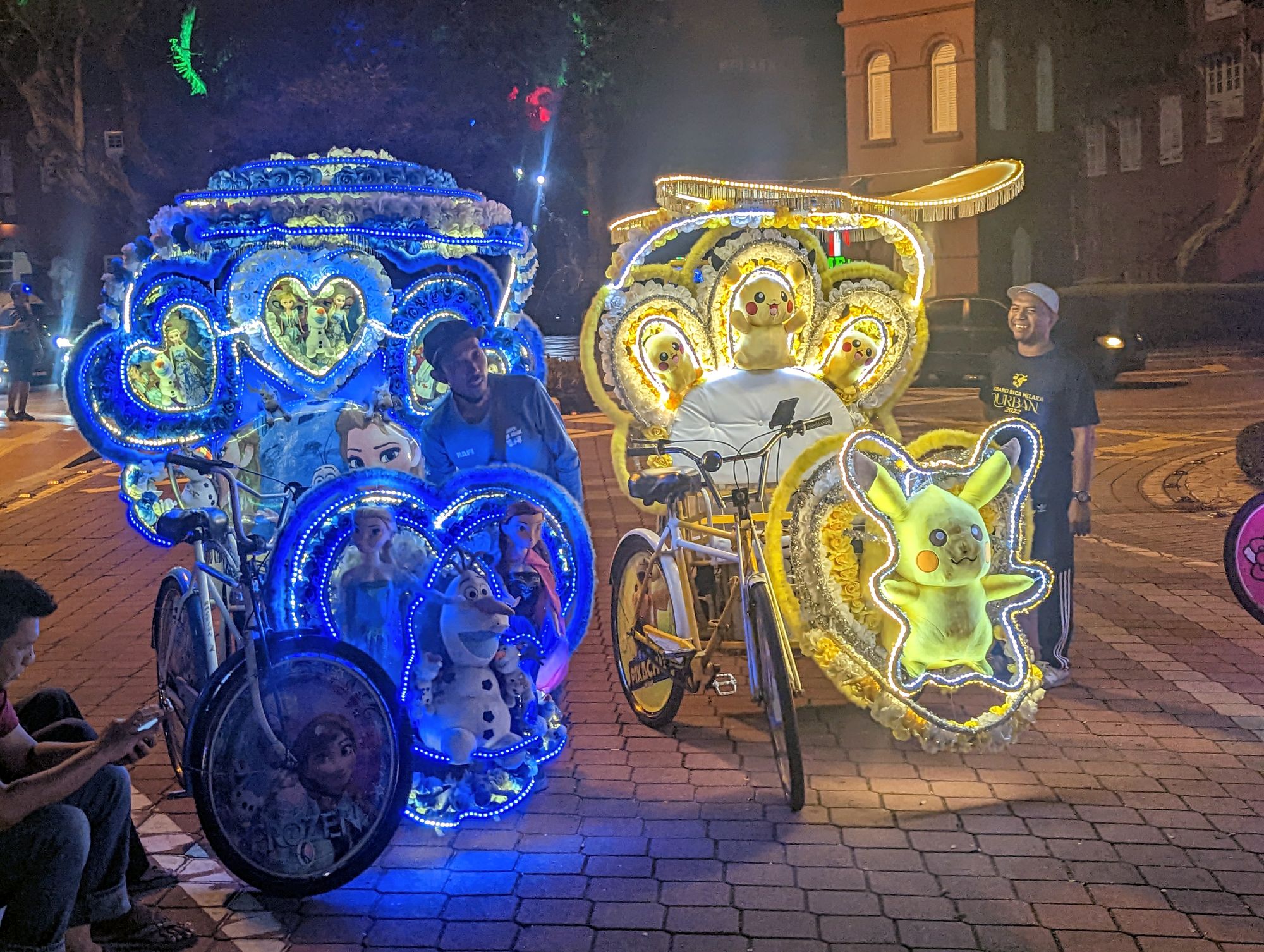 Two heavily decorated rickshaws on the street, one with Frozen move paraphernalia, and the other with Pikachu themed.